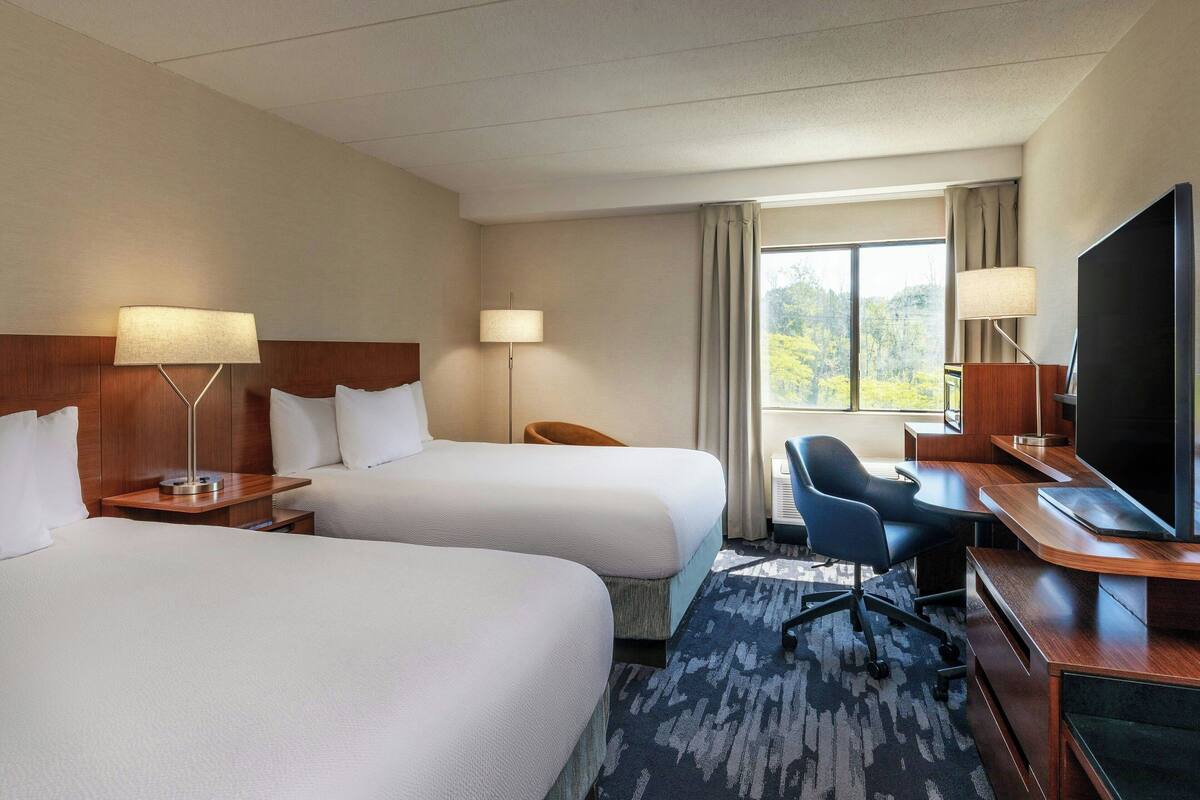 Een hotelkamer met twee bedden, een bureau met een computer, een televisie en een raam met gordijnen.