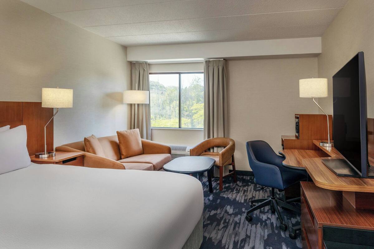 Een hotelkamer met een groot bed, een bureau met een televisie, een stoel, een bijzettafeltje en twee lampen.