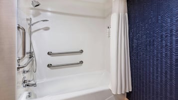 Un baño moderno con una bañera blanca, barras de apoyo, un cabezal de ducha manual y una cortina de ducha azul estampada.