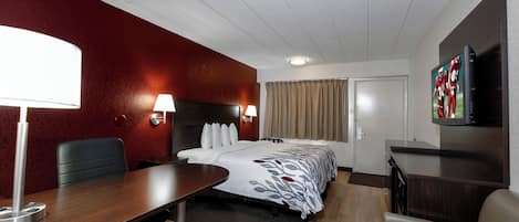 A hotel room with a bed, bedside lamps, a desk, a chair, a television, and a door.