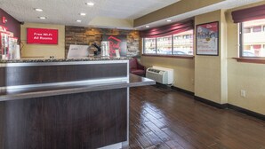 A hotel reception area with a counter, a sign indicating free Wi-Fi in all rooms, a Red Roof sign, and a window with a view of the outside.