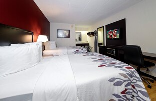 Habitación de hotel con una cama grande, un escritorio, una silla, un televisor y un espejo.