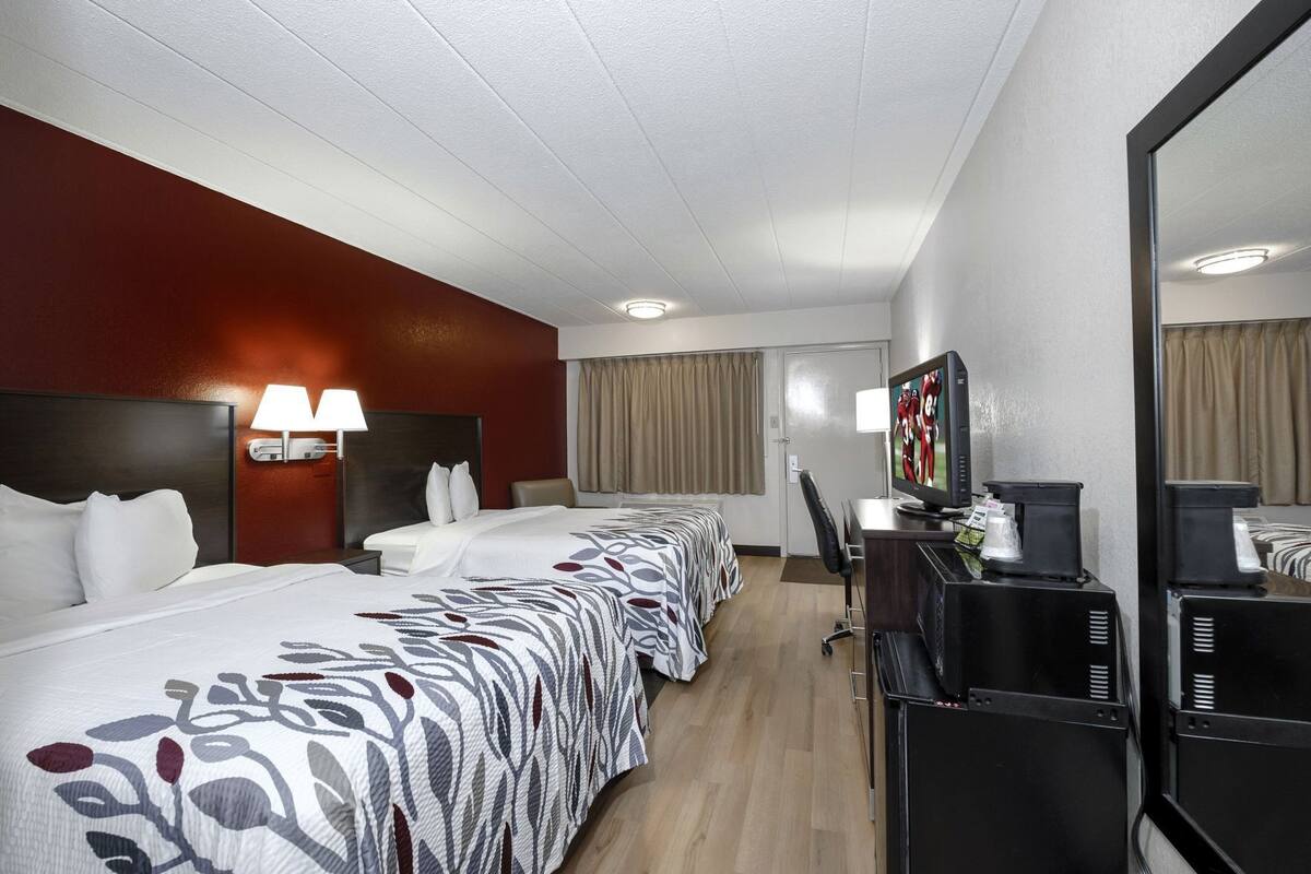 A hotel room with three beds, a desk with a computer, a TV, and a minibar.