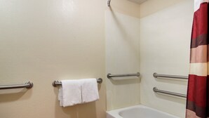 A bathroom with a bathtub, a shower curtain, and handrails.