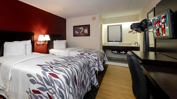 A hotel room with two beds, a desk, a mirror, a TV, and a bathroom.
