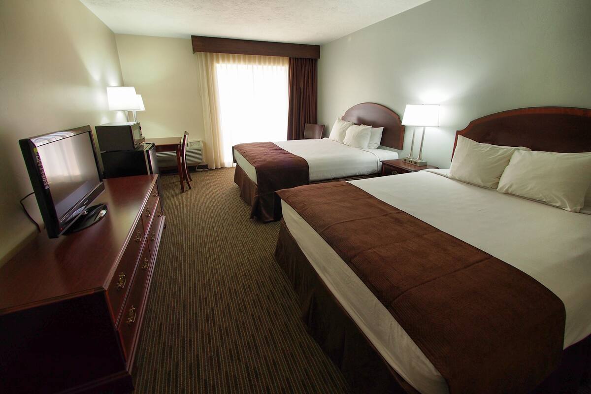 A hotel room with two beds, a desk with a TV, a chair, and a window with curtains.