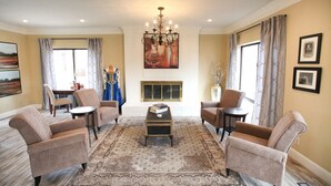 A spacious living room with a chandelier, comfortable seating, a fireplace, and artwork on the walls.