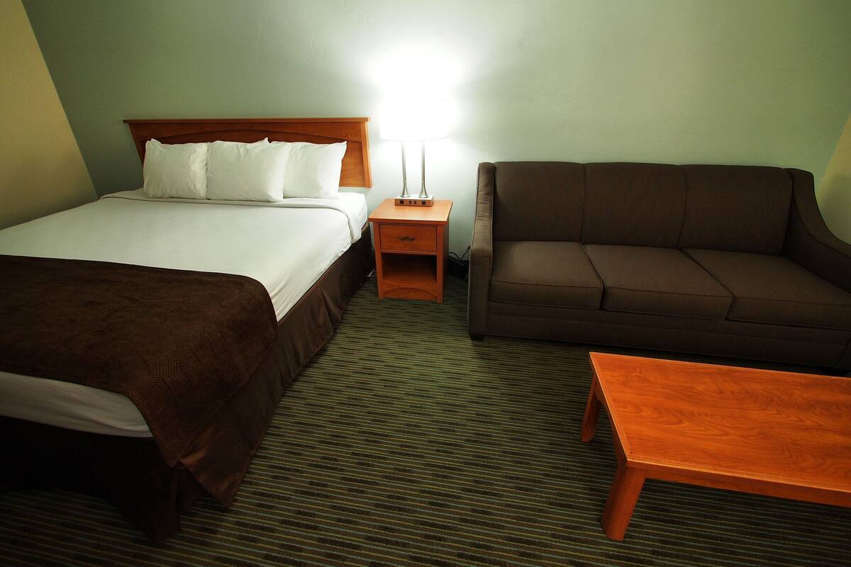 A hotel room with a bed, a sofa, a nightstand, and a small table.
