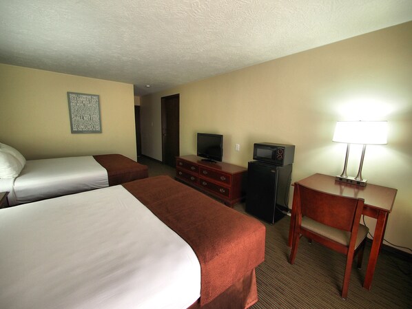 A hotel room with two beds, a TV, a refrigerator, a desk with a lamp, and a door leading to another room.