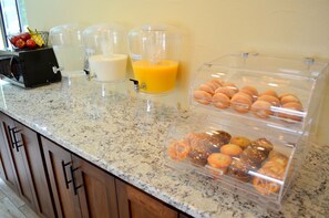 A breakfast bar with a juice dispenser, milk dispenser, and a display case with pastries.