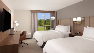 A hotel room with two beds, a desk, a chair, a TV, and a window with a view of trees.