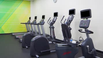 A row of stationary bikes in a gym with a green and white wall, a clock, and a water bottle on one of the bikes.