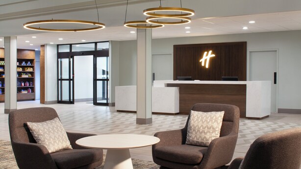 A modern lobby with a reception desk, two armchairs, a small table, and a patterned rug. - Holiday Inn Corpus Christi Arpt & Conf Ctr by IHG (Corpus Christi)