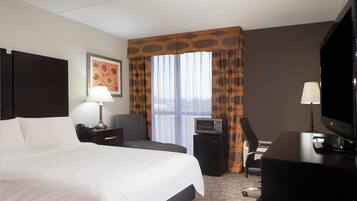 Une chambre d’hôtel avec un grand lit, un bureau avec une télévision, une chaise, une lampe de bureau et une fenêtre avec des rideaux.