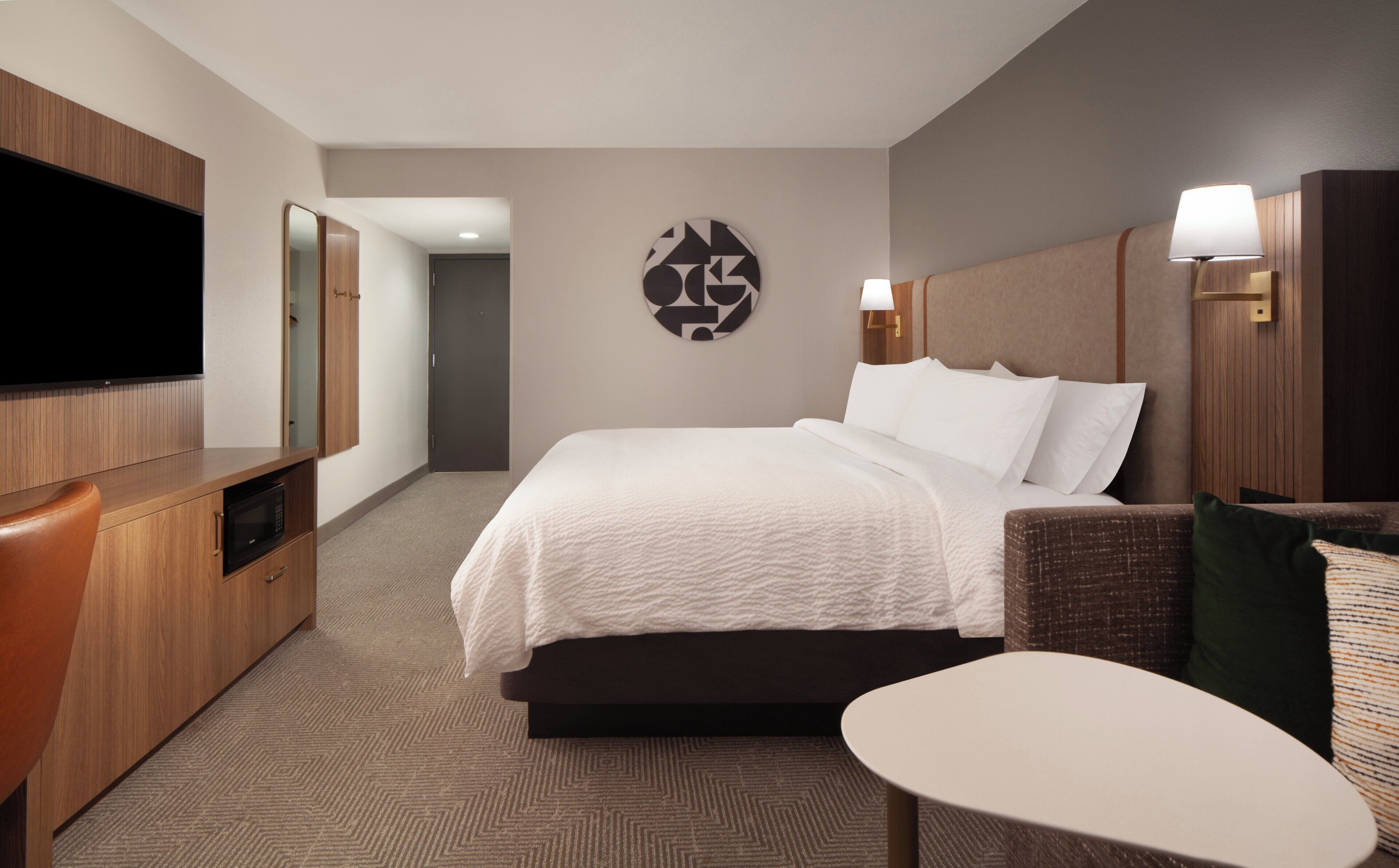 A hotel room with a bed, a TV, a desk, and a chair.