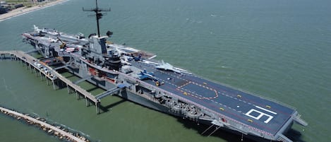 An aircraft carrier docked at a pier with a clear view of the deck and surrounding water.