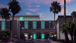 Un hotel Holiday Inn con facciata moderna, palme e ingresso ben illuminato.