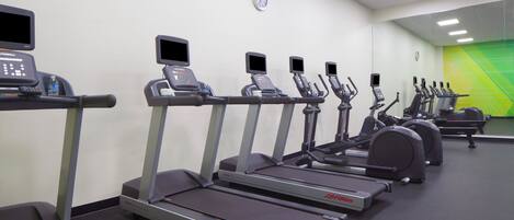 A gym with treadmills, ellipticals, and a water bottle on a bench.