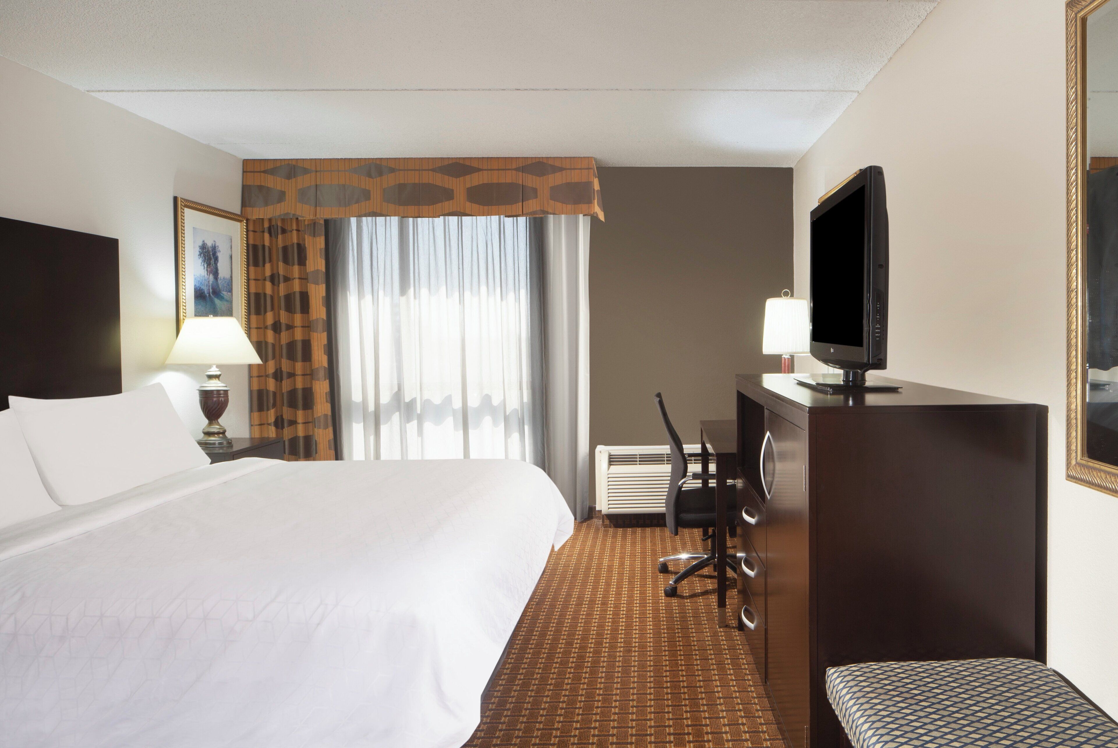 A hotel room with a large bed, a desk with a chair, a television, and a window with curtains.