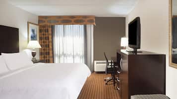 A hotel room with a large bed, a desk with a chair, a television, and a window with curtains.