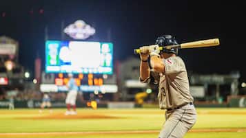 Un jugador de béisbol en un estadio, con un marcador digital grande al fondo.