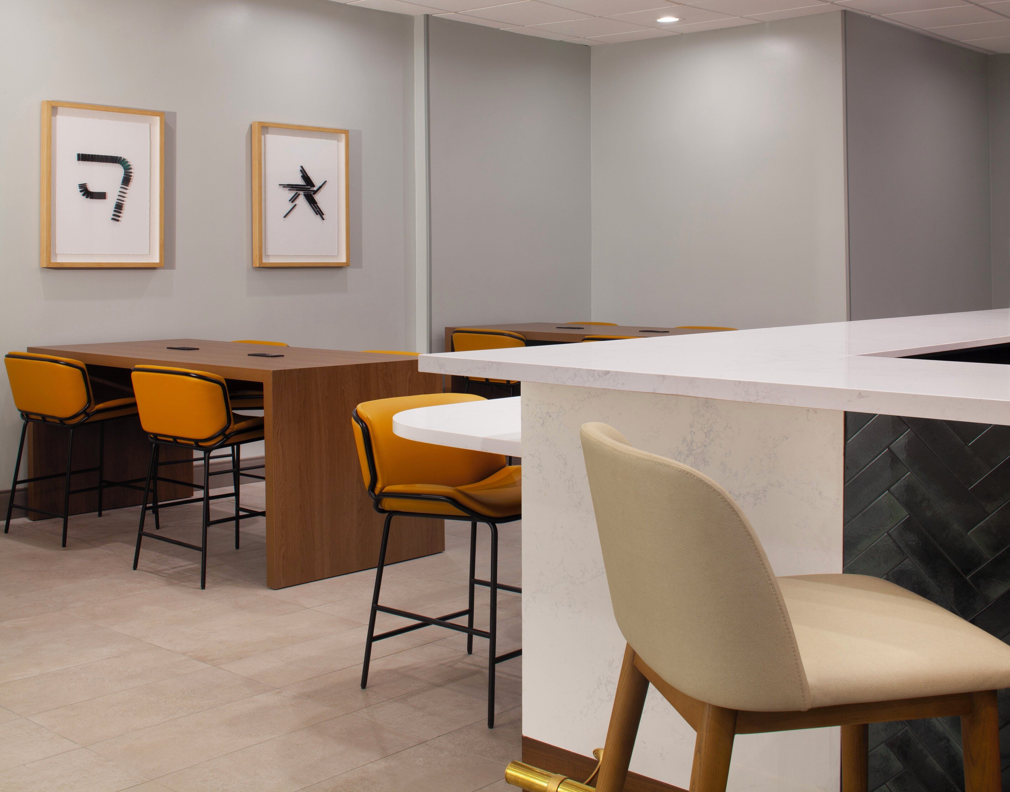 A modern dining area with a wooden table and yellow chairs, a white counter, and two framed abstract art pieces on the wall.