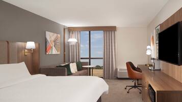 Habitación de hotel con una cama grande, un sofá, un escritorio, un televisor y una ventana con cortinas.