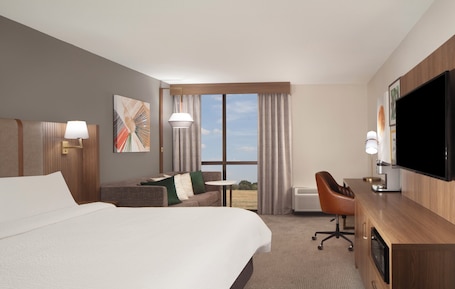 A hotel room with a large bed, a sofa, a desk, a television, and a window with curtains.