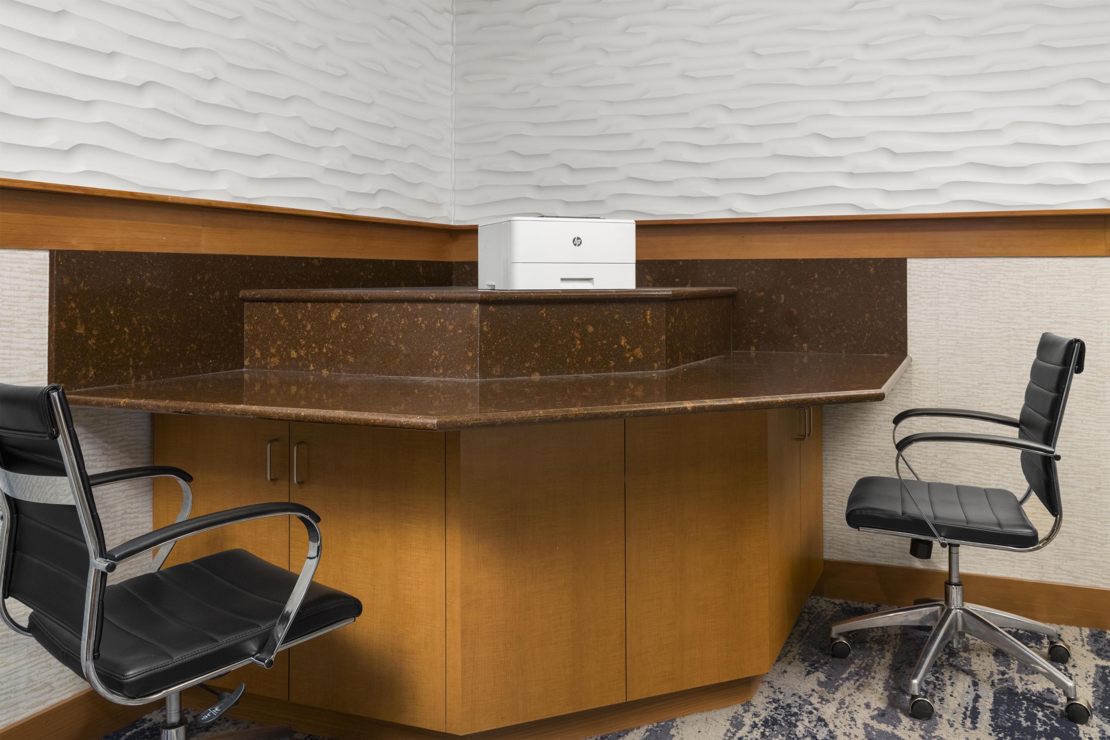 A corner office with a wooden desk, two black office chairs, and a white HP printer.