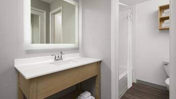A modern bathroom with a white sink, wooden vanity, and a glass shower enclosure.