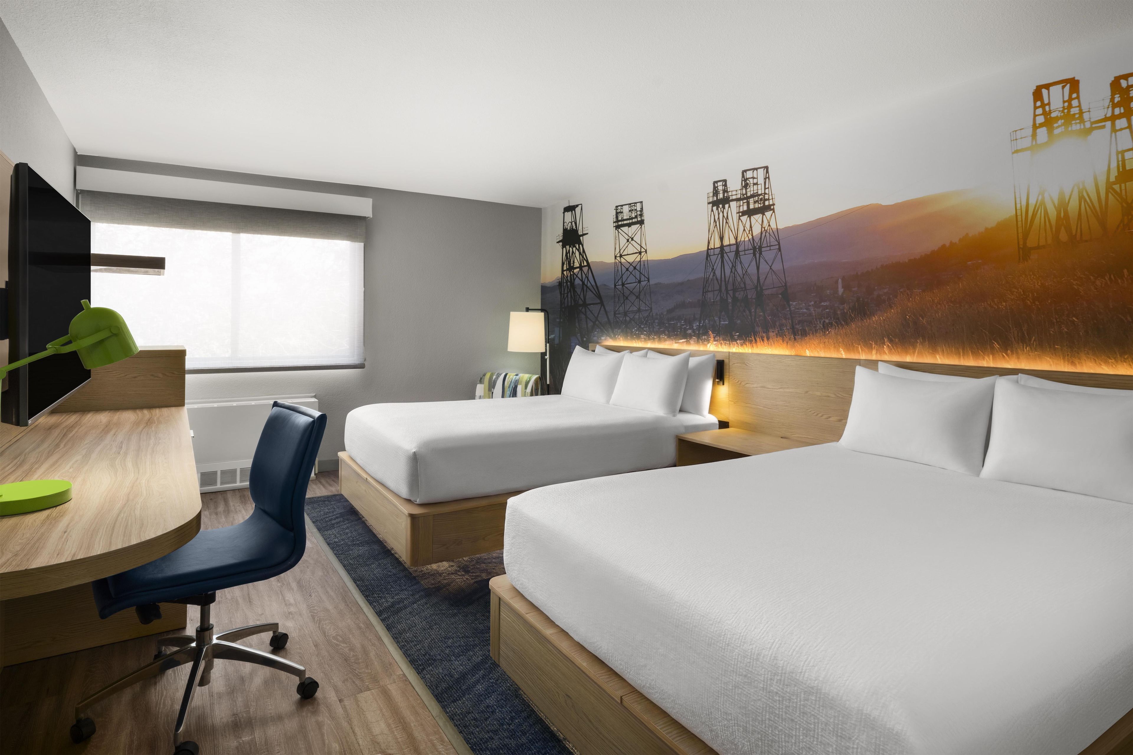 A hotel room with a bed, a desk, a chair, a lamp, and a large wall mural.