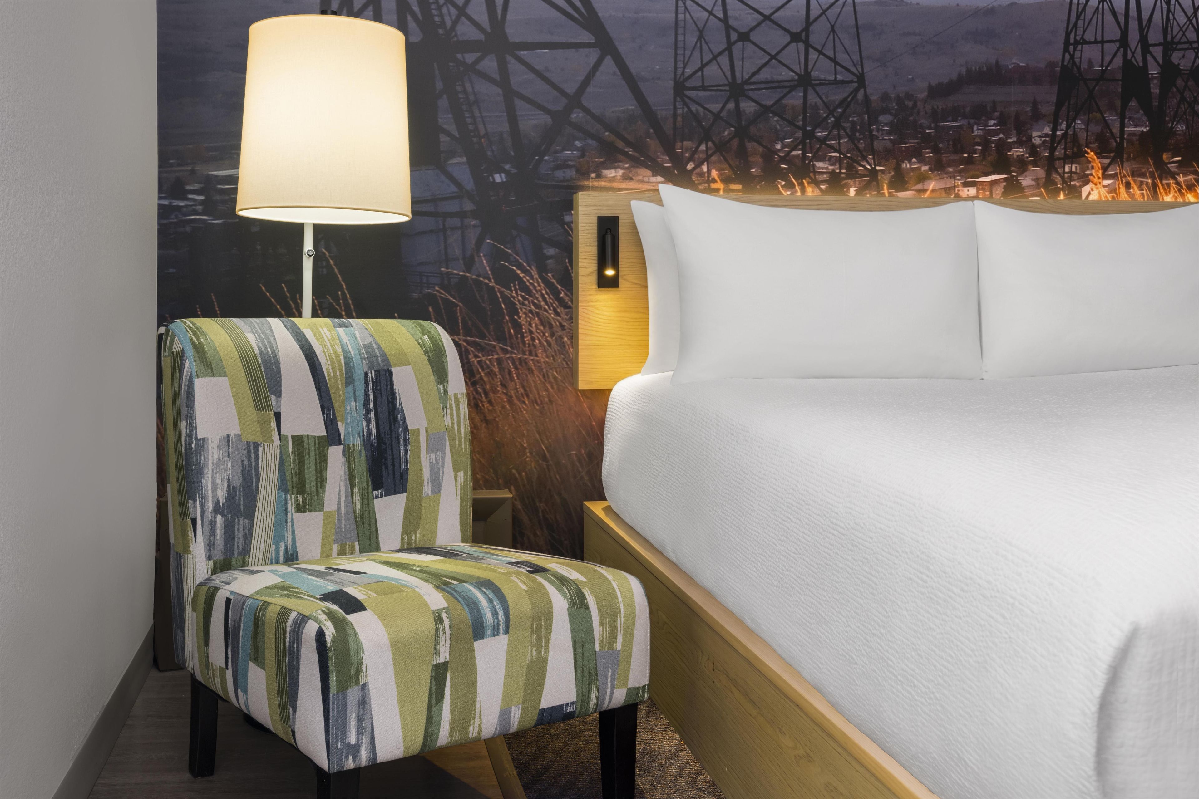 A hotel room with a bed, a nightstand, a lamp, and a chair.