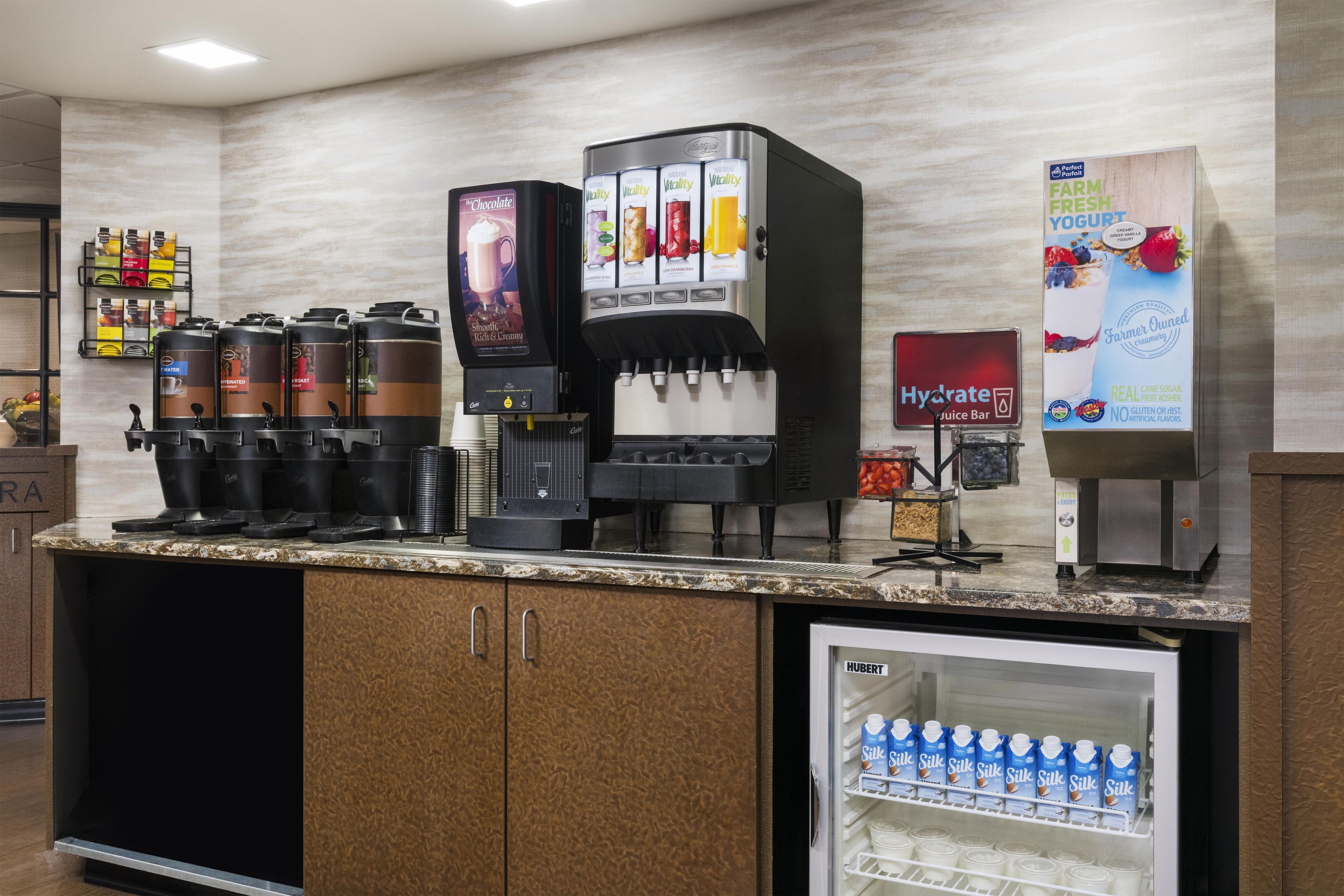 A self-service beverage station with multiple coffee machines, a water dispenser, and a refrigerated drink cooler.