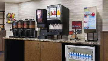 A self-service beverage station with multiple coffee machines, a water dispenser, and a refrigerated drink cooler.