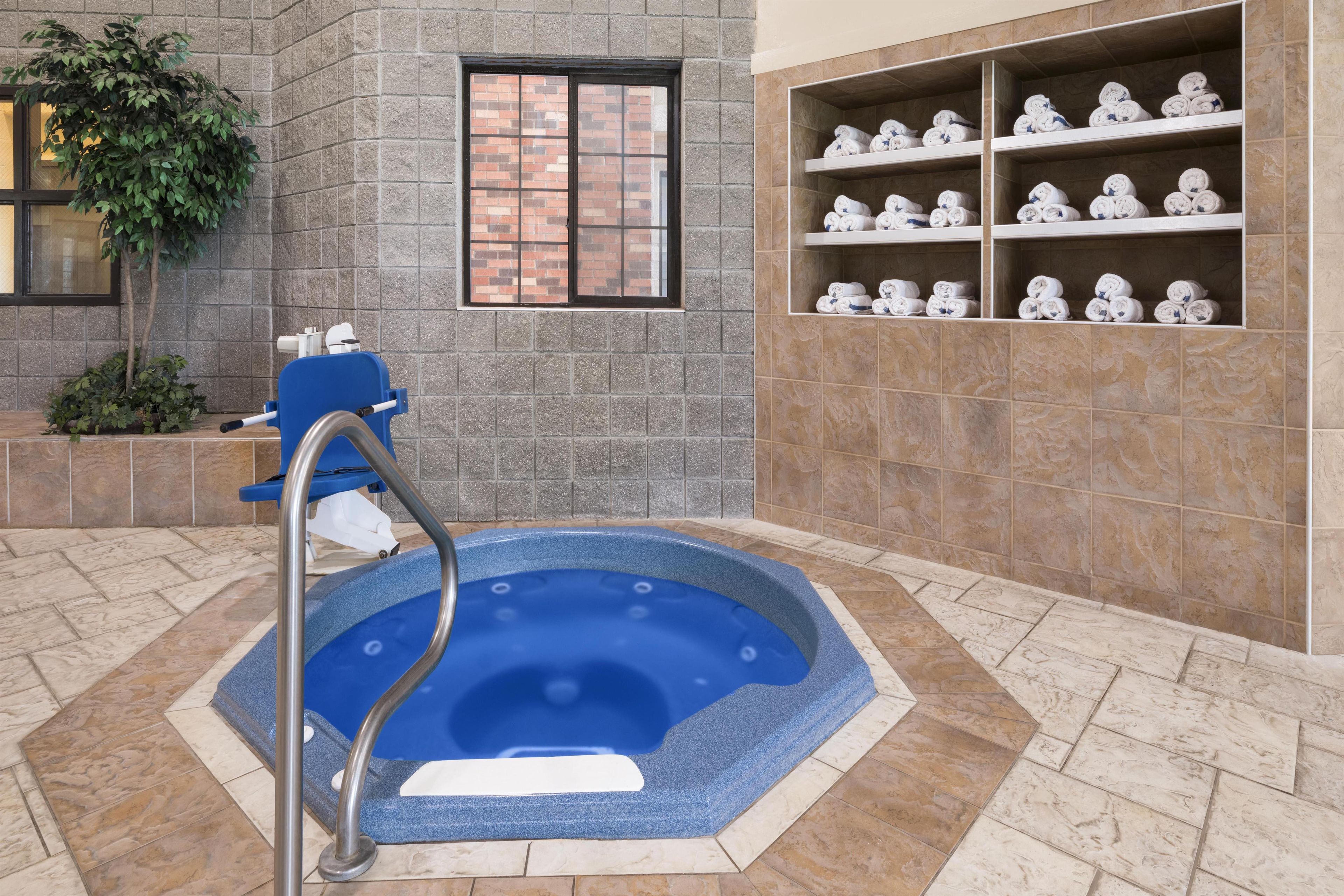 Een wellnessruimte met een jacuzzi, een raam en planken met handdoeken.
