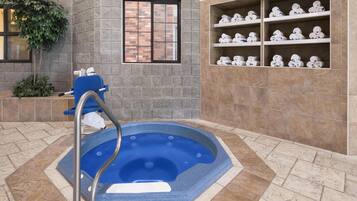 Een wellnessruimte met een jacuzzi, een raam en planken met handdoeken.