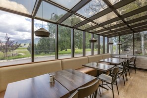 A restaurant with a glass enclosure, wooden tables, and a bench.