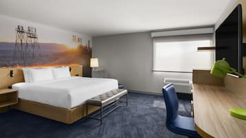 A hotel room with a bed, a desk, a chair, a lamp, and a window.