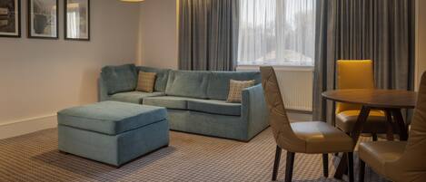 Una sala de estar con sofá, reposapiés y sillas, una mesa de comedor y una ventana con cortinas.