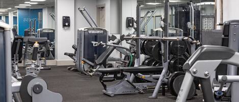 A gym with various exercise equipment, a blue wall with the word 'TITANIC' visible, and a mirrored wall.