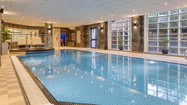 An indoor swimming pool with tiled walls, a tiled floor, and a glass door leading to a changing room. - DoubleTree by Hilton Stoke on Trent (Stoke-on-Trent)