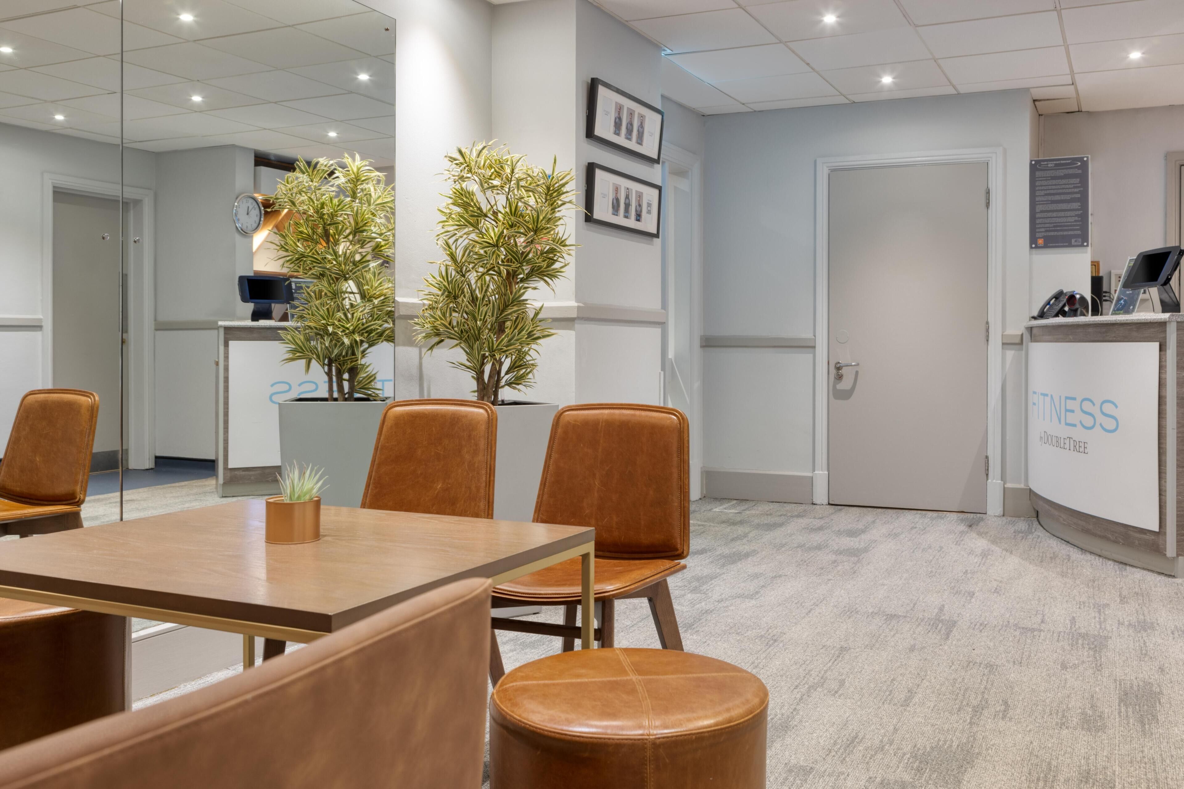Un salón de conferencias con una mesa de madera, sillas de cuero y plantas en macetas.