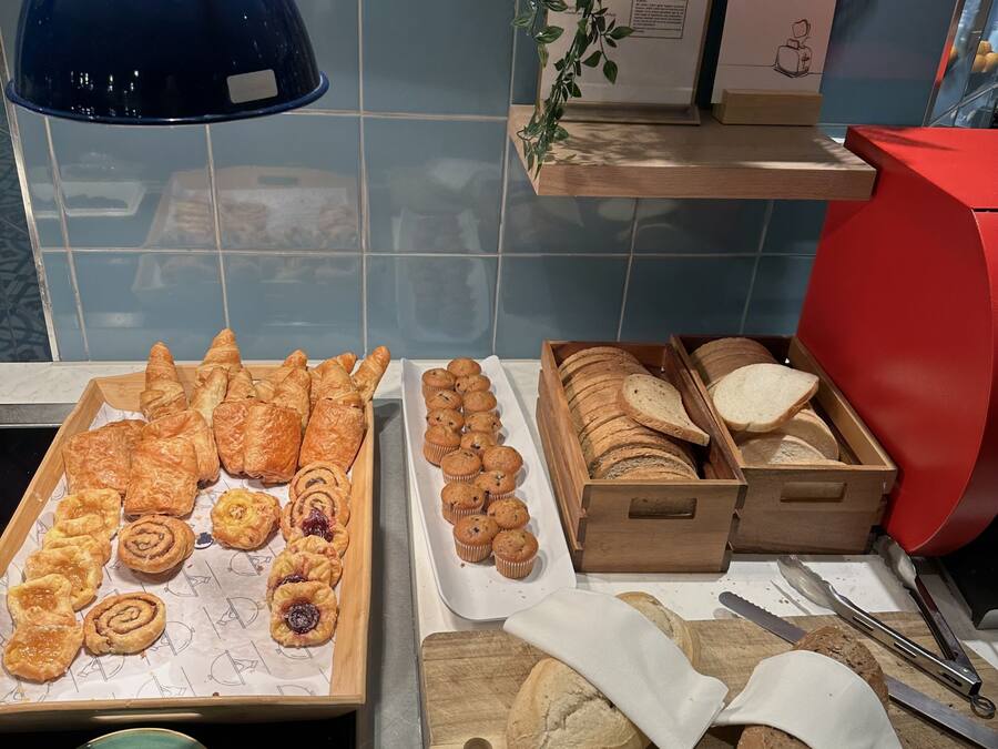Mostrador de panadería con diversos pasteles y pan, una lámpara azul y una pizarra con el menú.