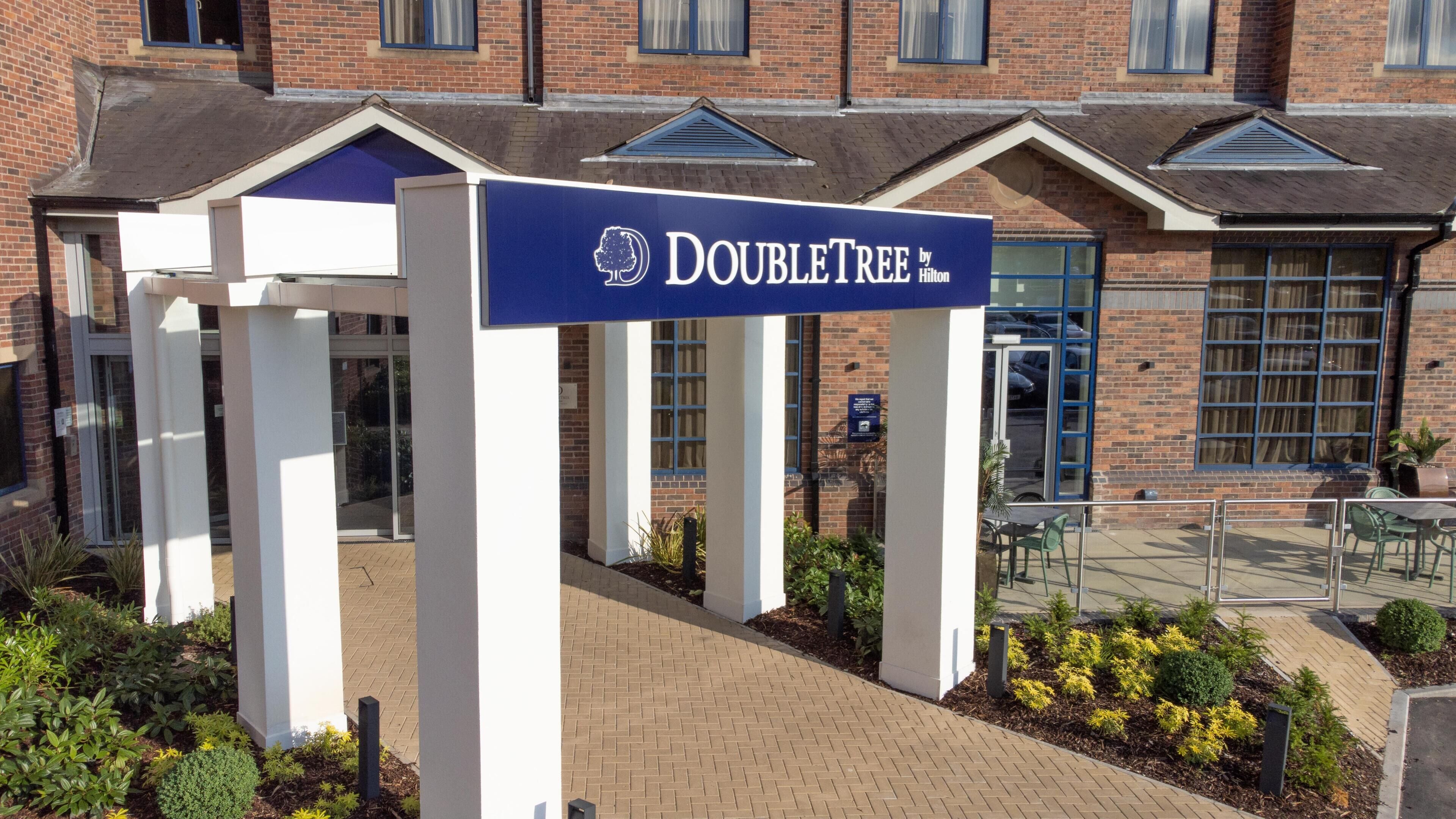 A DoubleTree by Hilton hotel entrance with a brick facade, large windows, and a covered outdoor seating area.