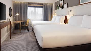 Ett hotellrum med två sängar, ett skrivbord, en stol, en TV och ett fönster med gardiner.