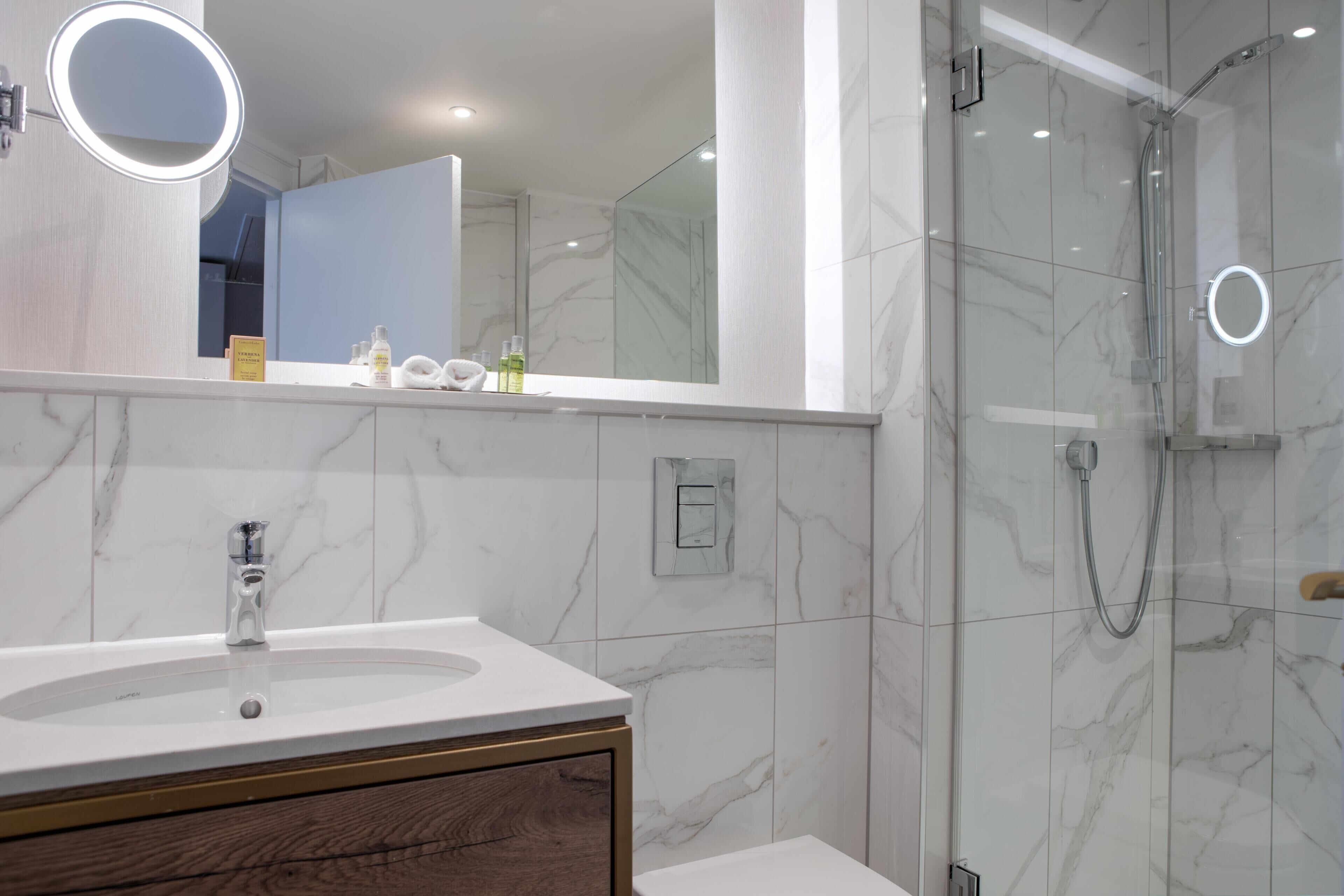 Un baño con lavamanos de mármol, un espejo con luz y una ducha con cerramiento de vidrio.