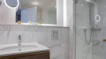 Un baño con lavamanos de mármol, un espejo con luz y una ducha con cerramiento de vidrio.