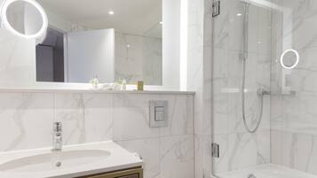 A modern bathroom with a marble sink, a mirror with a light, and a glass-enclosed shower.