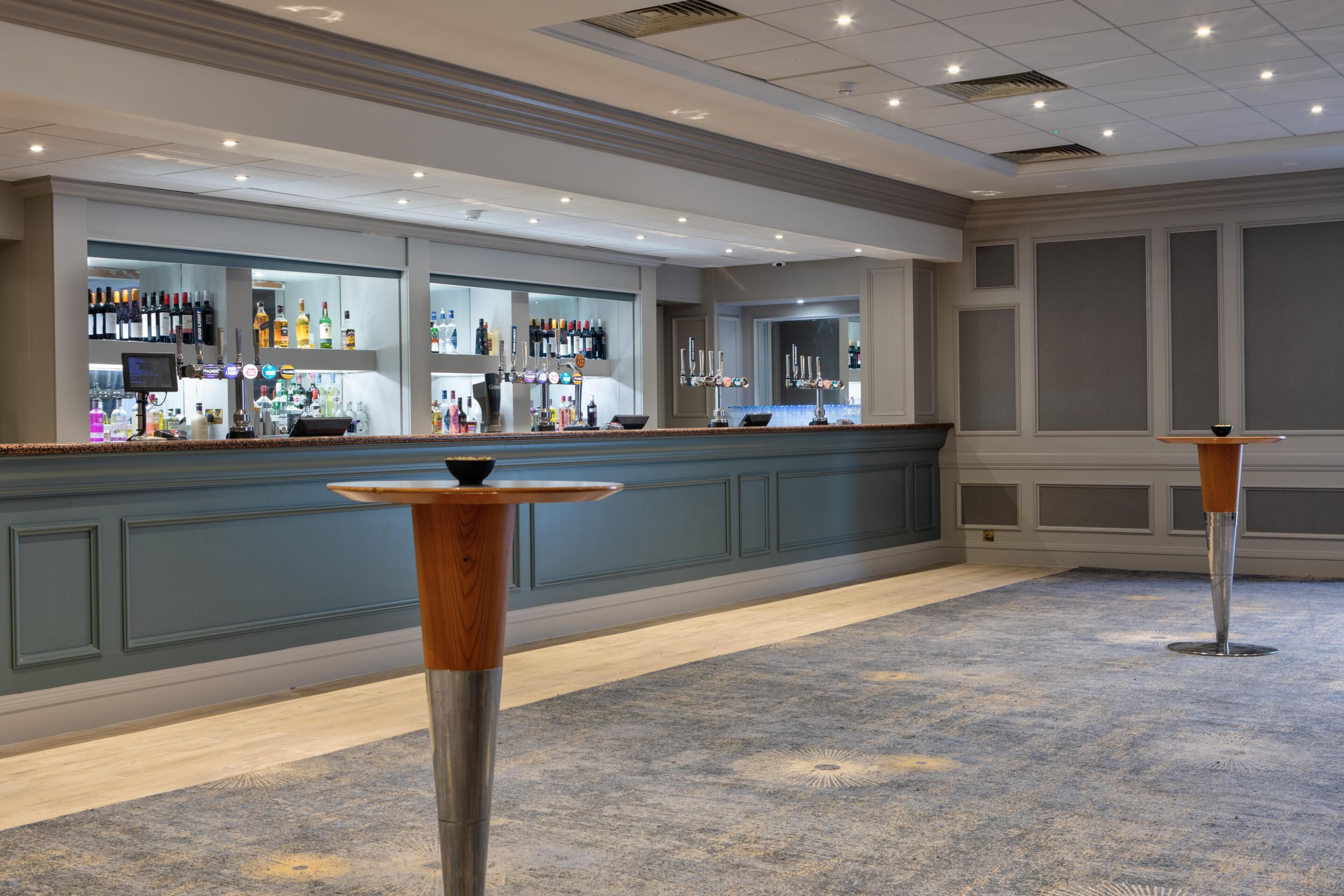 A bar area with a counter, bar stools, and a variety of bottles and glasses.