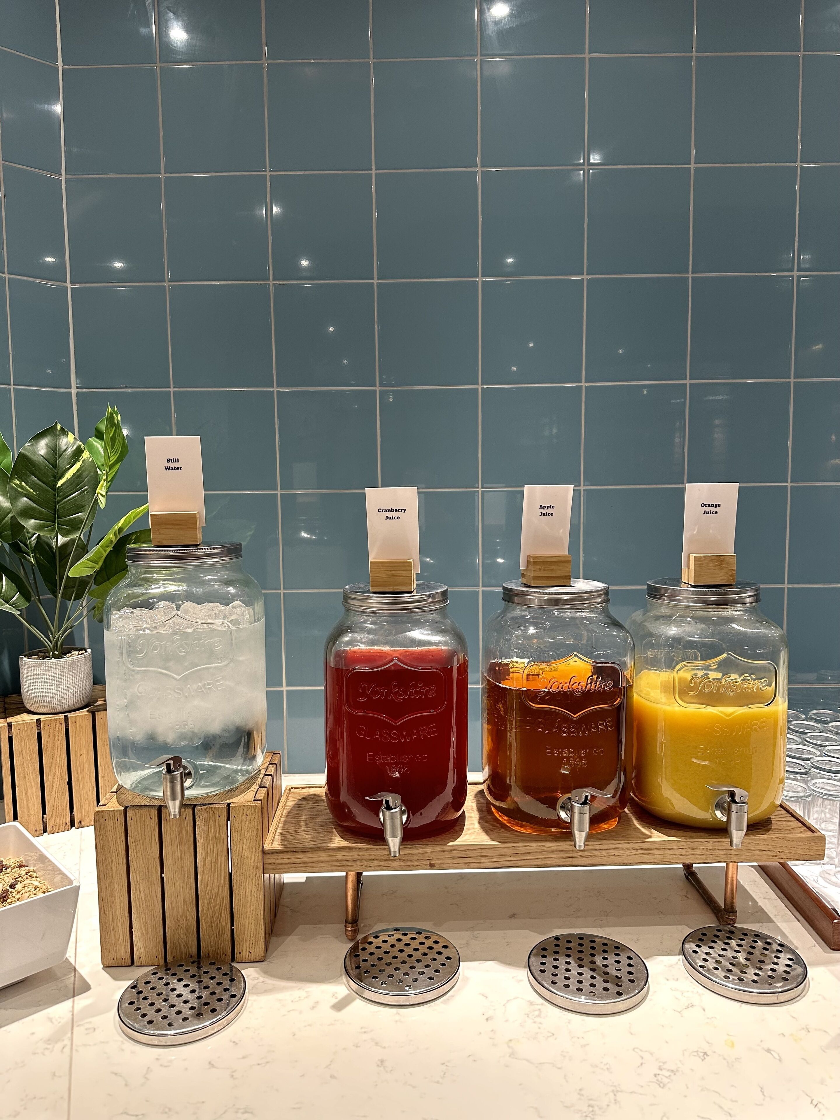 Four glass jars with taps on a wooden stand, each labeled with a different juice type.